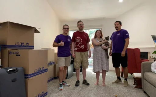 Double Move moving crew in purple uniforms with boxes in front of a company moving truck before a long distance move