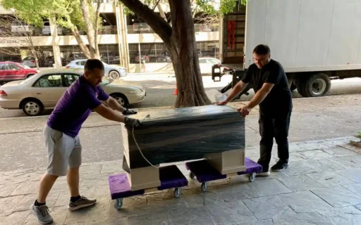 Two Double Move movers rolling a shrink-wrapped piece of furniture on dollies to the moving truck